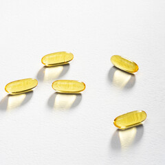 Sunlight passes through a few Omega-3 capsules lying on a white background. Caustics light. Fish oil pills. Medical support and treatment. Biologically active additives. Wellness and self care. Square