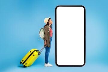 Black female traveler with suitcase and backpack looking at big smartphone with mockup for online...