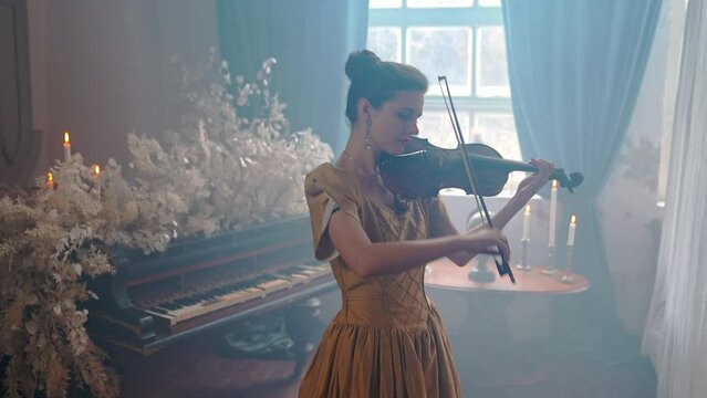 A Young Girl And Man Plays The Violin In A Beautiful Retro Room With Flowers And A Piano.