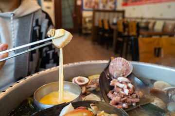 A woman is picking up a slice of boiled clams and cheese sauce with chopsticks.