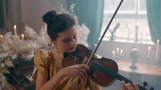 A Young Girl And Man Plays The Violin In A Beautiful Retro Room With Flowers And A Piano.