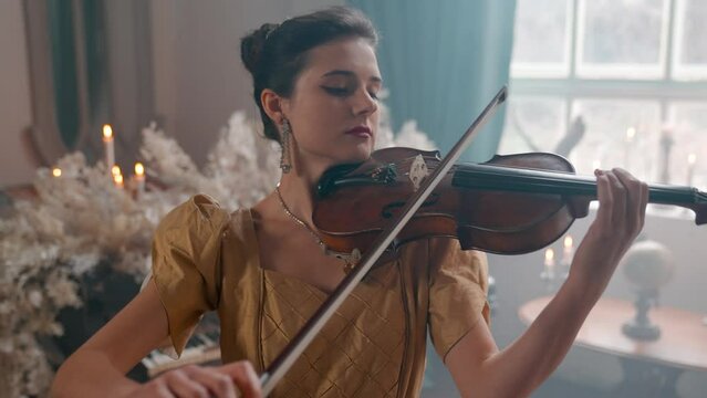 A Young Girl And Man Plays The Violin In A Beautiful Retro Room With Flowers And A Piano.