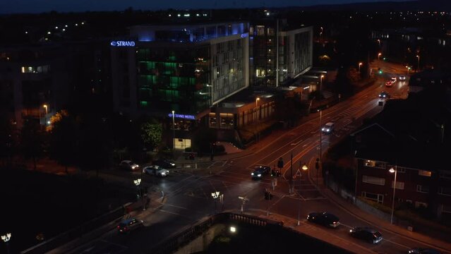 Elevated shot of cars passing through crossroads in night city. Colour illuminated building on corner. Limerick, Ireland