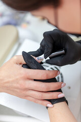 Manicure master, working in the beauty salon covering   nails of     female client with gel polish