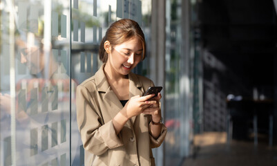 Happy young smiling Asian woman standing using a mobile phone