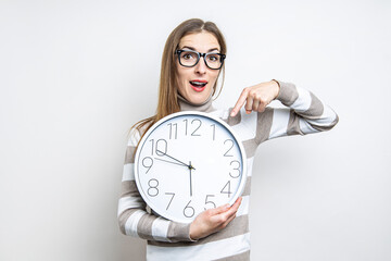 Surprised young woman pointing at wall clock on light background.