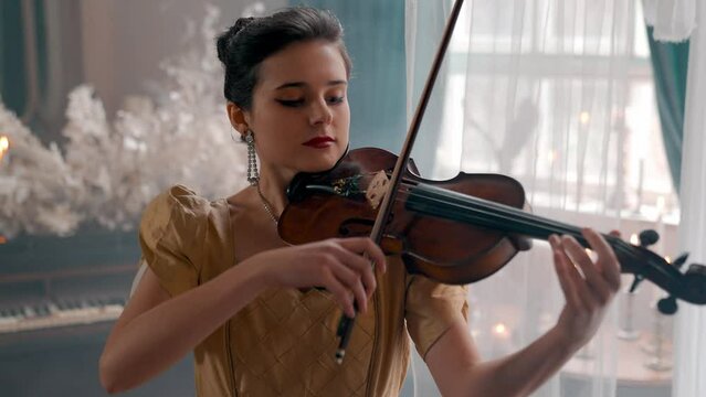 A Young Girl And Man Plays The Violin In A Beautiful Retro Room With Flowers And A Piano.  Ypung Girl.