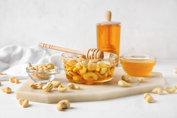 Bowl of sweet cashew nuts and honey on light background