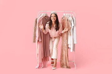 Beautiful young girl near rack with clothes for high school prom on pink background