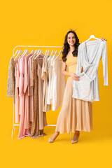 Beautiful young girl near rack with clothes for high school prom on yellow background