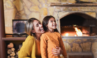 Loving mother hugging little daughter at home on patio next to the fireplace