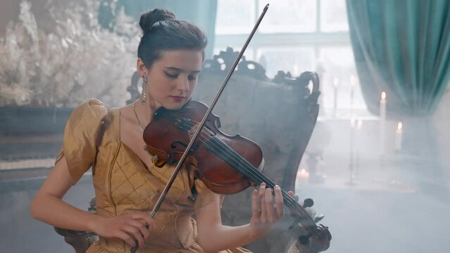 A Young Girl And Man Plays The Violin In A Beautiful Retro Room With Flowers And A Piano. 