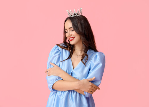 Beautiful young woman in stylish dress and tiara on pink background
