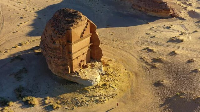 Aerial view overlooking a person running in front of the Hegra monument, in sunny Saudi Arabia - tilt, drone shot