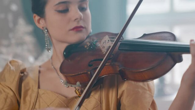 A Young Girl And Man Plays The Violin In A Beautiful Retro Room With Flowers And A Piano.