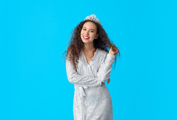 Beautiful young African-American woman in stylish dress and tiara on blue background