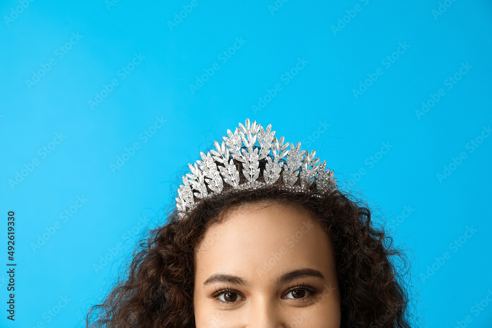 Wall mural Beautiful young African-American woman in stylish tiara on blue background