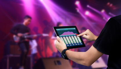 Sound Engineer using digital tablet to remote sound,audio mixer control on blurred concert as...