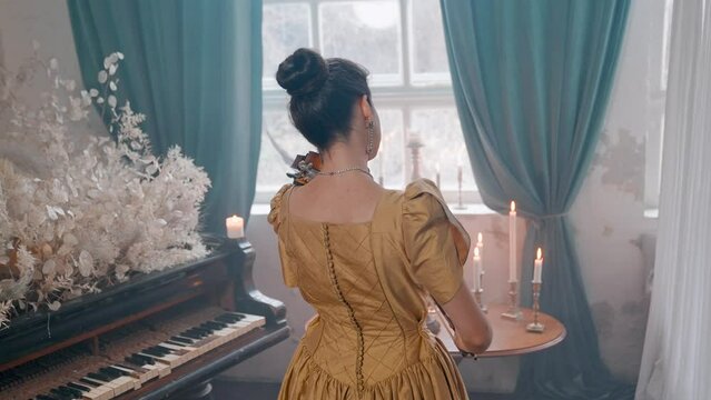 A Young Girl And Man Plays The Violin In A Beautiful Retro Room With Flowers And A Piano.