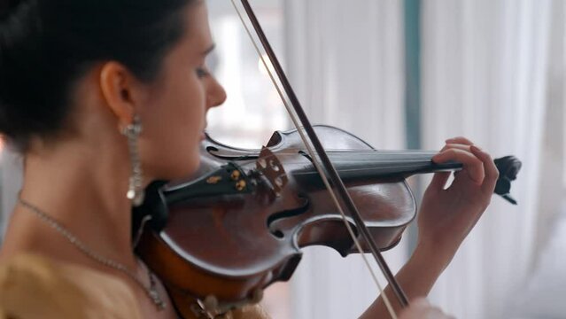A Young Girl And Man Plays The Violin In A Beautiful Retro Room With Flowers And A Piano.