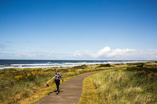 A man carrying a surfboard walks down a path toward the beach