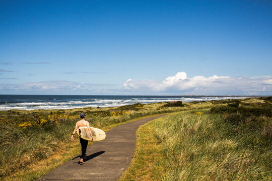 A man carrying a surfboard walks down a path toward the beach