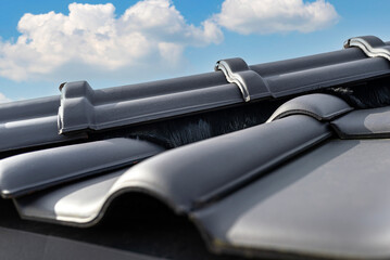 Ridge tile on the roof of a single-family house covered with a new ceramic tile in anthracite against the blue sky.