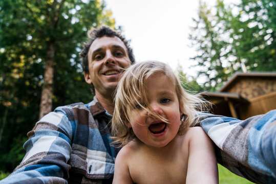 A dad takes selfie with shirtless child in forest