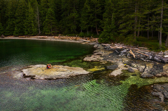 A family sits on rock surrounded by clear green water and forests