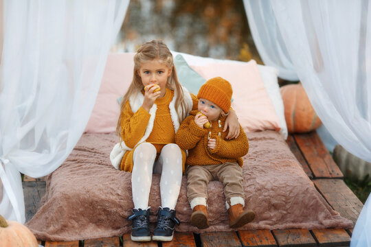 Cute Small Baby Boy And His Sister Eating Pear In Ginger Sweaters And Knit Hats On Sunny Autumn Day. Family Time At Thanksgiving. Festive Season Of Harvest. 