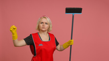 angry cleaning lady in an apron and gloves waving a broom on a colored background