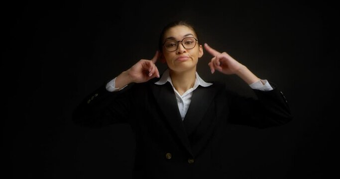 Businesswoman in glasses and office clothes does not want to listen to the interlocutor, plugs ears and says blah, blah, blah.An attractive Asian woman doesn't want to hear anything.Black background.