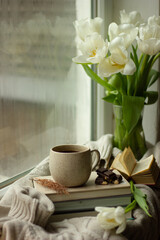 Cup of coffee and knitted sweater near window in morning. Space for text