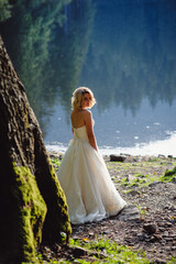 Bride in white wedding dresses on rocky shore near lake in mountains. Wedding on a background of mountain landscape. Picturesque view of the mountain.