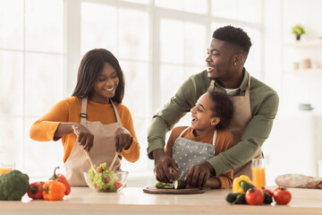 Black Parents And Daughter Cooking Making Vegetable Salad In Kitchen