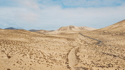 Path road in the middle of a mountains sand desert with blue bright sky in background. Concept of desertification or climate change for global warming. Amazing scenic travel destination
