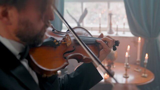 A Young Girl And Man Plays The Violin In A Beautiful Retro Room With Flowers And A Piano.