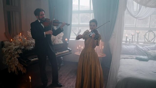 A Young Girl And Man Plays The Violin In A Beautiful Retro Room With Flowers And A Piano.