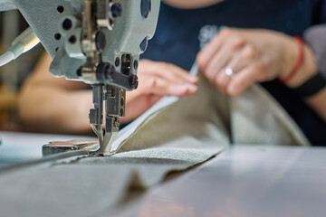 Process of a seamstress sewing beige fabric in a sewing workshop. The needle of the sewing machine is in motion. The process of sewing fabric. 