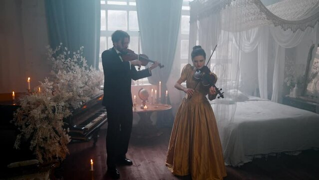 A Young Girl And Man Plays The Violin In A Beautiful Retro Room With Flowers And A Piano.