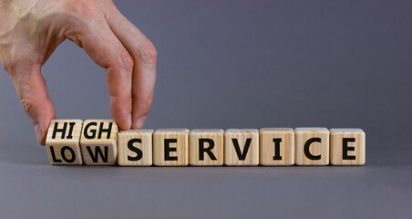 Low or high service symbol. Businessman turns cubes and changes words low service to high service. Beautiful grey table grey background. Business low or high service concept, copy space.