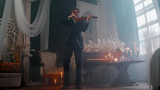 A Young Girl And Man Plays The Violin In A Beautiful Retro Room With Flowers And A Piano.