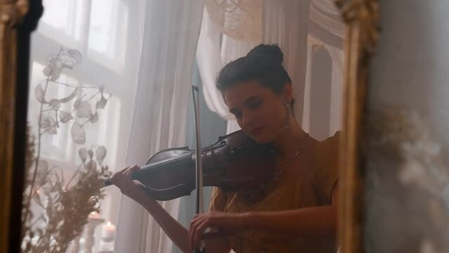 A Young Girl And Man Plays The Violin In A Beautiful Retro Room With Flowers And A Piano.