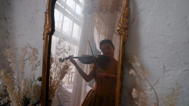 A Young Girl And Man Plays The Violin In A Beautiful Retro Room With Flowers And A Piano.