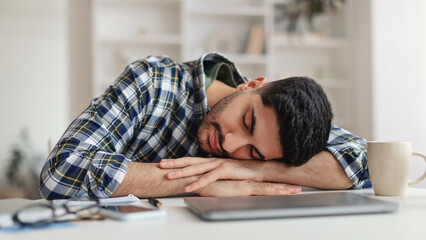 Fototapeta premium Exhausted Young Man Sleeping At Work Sitting At Desk