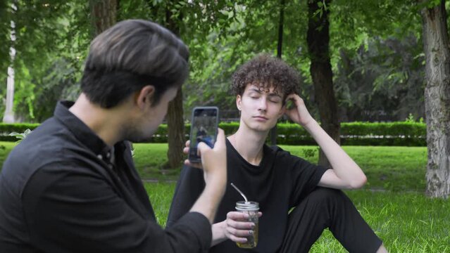 A guy takes pictures on the phone of another guy in nature in the summer. LGBT