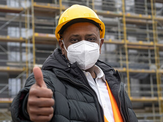 Successful Indian construction worker wearing a protective ffp2 mask posing on construction site showing thumbs up gesture