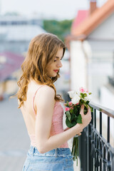 A beautiful young girl in light clothes holds a bouquet of roses in her hands