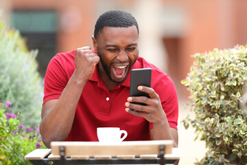 Excited man with black skin checking phone in a bar