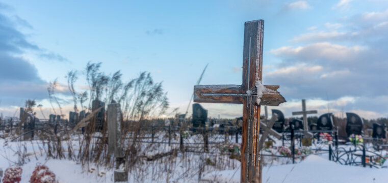 Snowy old broken grave wooden cross shaped on dramatic sky background. Orthodox traditional cemetery in snowy winter.